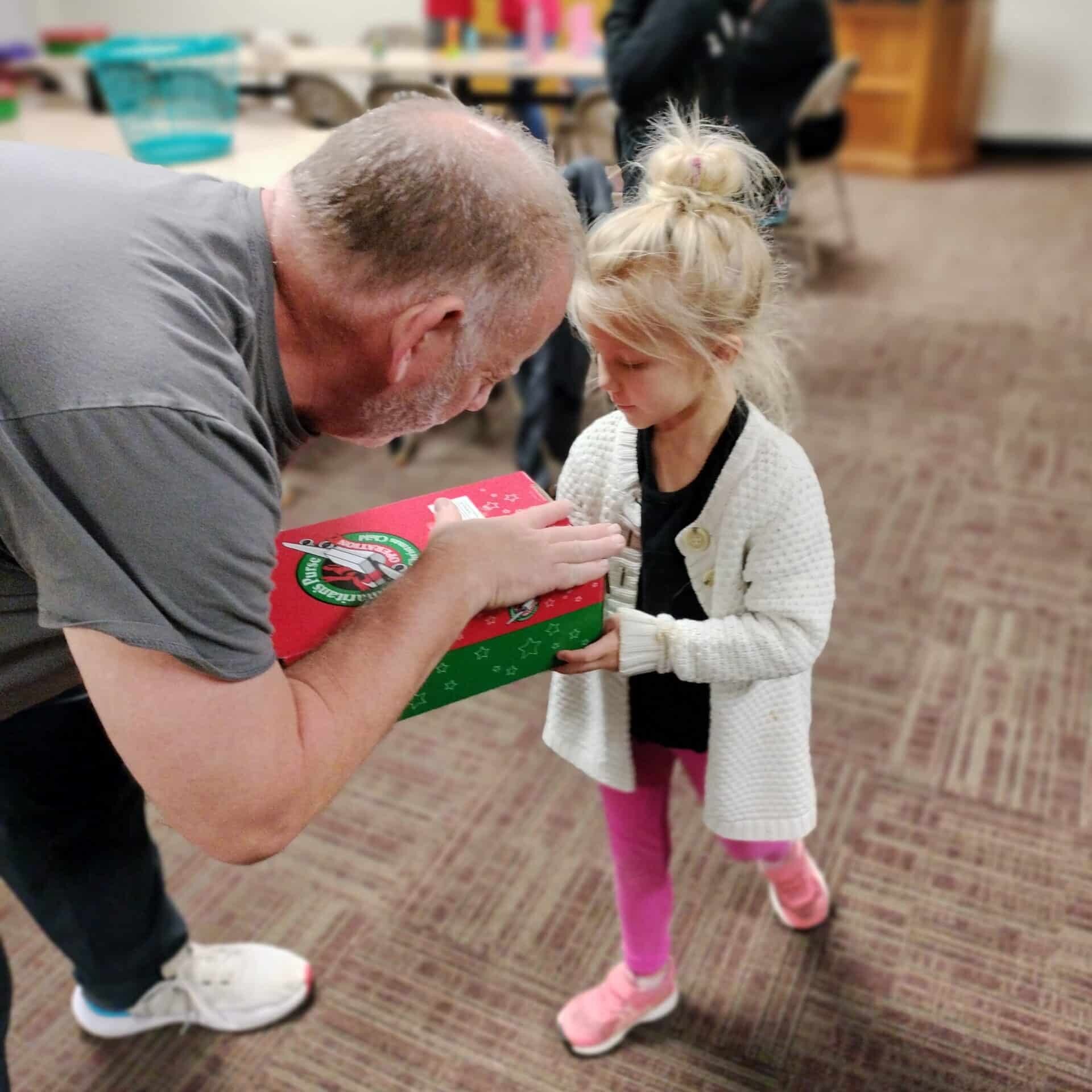 a man and little girl praying over red and green Christmas box
